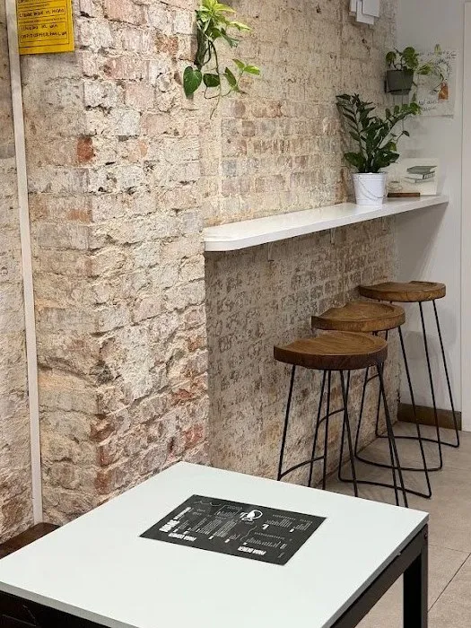 Rincón del local con pared de ladrillo encalado, barra de madera con taburetes, plantas y una mesa alta